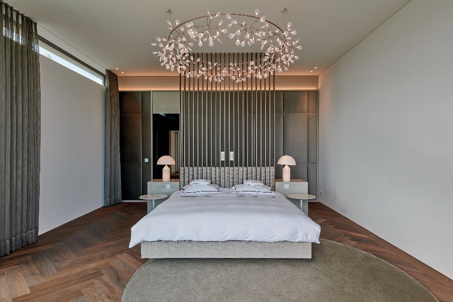 Dunkler Fischgrätparkett ist ein wesentliches Element der gesamten Raumästhetik, genauso wie die markanten Leuchtendesigns. Hier zu sehen im Schlaf- und Ankleidezimmer. Copyright: VINOVA Architects GmbH Fotograf: Holger Jacob